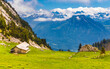 Beautiful view of a mountainous landscape with a wooden alpine hut surrounded by lush meadows and a wonderful view of the alps afar and the valley below in Central Switzerland.