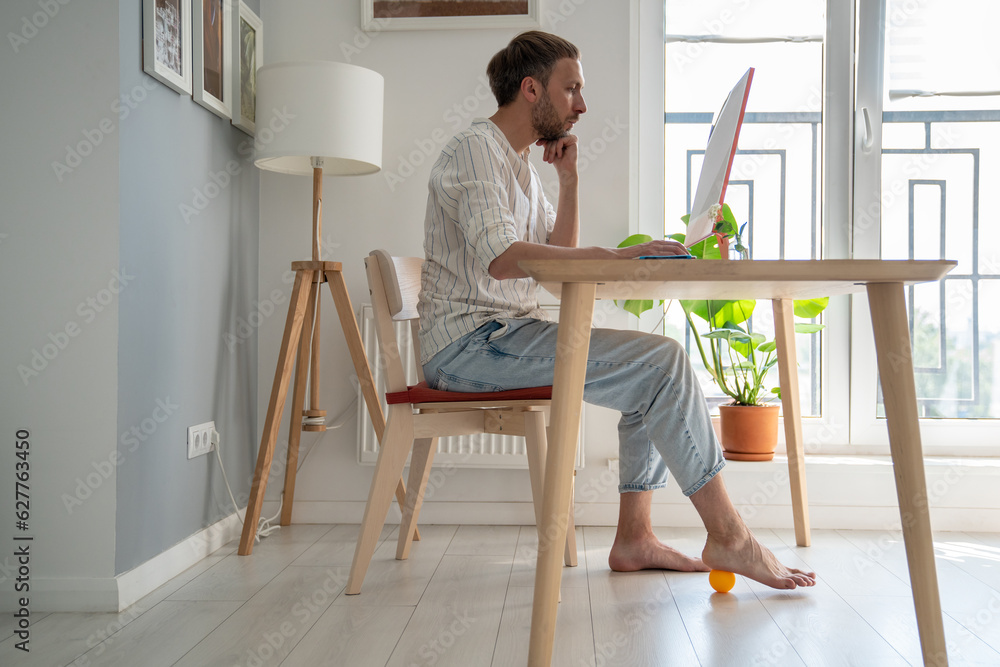 Man freelancer working on computer at home doing foot exercise using ...