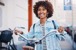 © Flamingo Images - Smiling woman wearing headphones pushing a bike along a sidewalk in the city