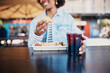© Flamingo Images - Smiling woman sitting at a table outdoors and eating tacos with a drink
