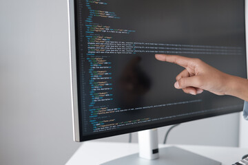 Close up view of programmer pointing to desktop computer with developing programming code, trying to solve the problem.