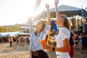 Wall Mural - Joyful two young girlfriends have fun with beer at the beach party. Happy two women enjoy the weekend at the music festival. The concept of friendship, holiday, weekend.