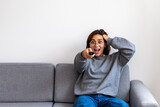 Fototapeta Paryż - black-haired woman in gray sweatshirt watching tv surprised