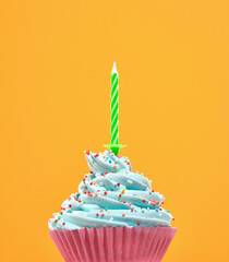 Birthday cupcake with blue cream and colored sprinkles. Green holiday candle. Celebration mood.