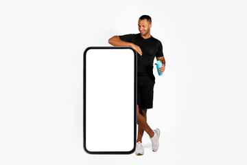 Wall Mural - Black fitness man standing near big mobile phone, white background