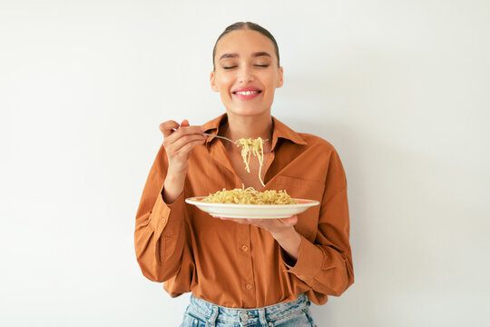 satisfied caucasian lady enjoying tasty italian spaghetti with closed eyes, standing on white studio