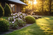 Beautiful Manicured Lawn And Flowerbed With Deciduous Shrubs On Private Plot And Track To House Against Backlit Bright Warm Sunset Evening Light On Background.