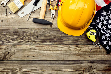 Wall Mural - Yellow hard hat, American flag, construction tools on wooden table. Labor day USA holiday greeting card template.