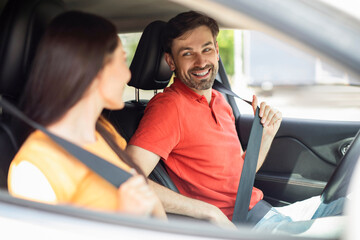 Happy beautiful lovers fasten seat belts in car, going vacation