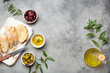 © somegirl - Sliced fresh ciabatta on cutting kitchen board, green and brown olives, olive oil with rosemary, olive tree branches on gray concrete stone rustic background from above copy space