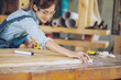 © EKKAPON - Attractive middle aged woman carpenter designer works with ruler, make notches on the tree in workshop. Image of modern femininity. Concept of professionally motivated women