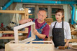 © EKKAPON - Portrait of senior carpenter teaching apprentice standing at table in workshop