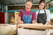 © EKKAPON - Senior male carpenter instructing young woman to use equipment while working at carpentry workshop.