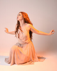 Poster - Full length portrait of beautiful brunette  female model wearing dress with golden back light lighting. Kneeling pose with gestural arm pose.  isolated on studio background.