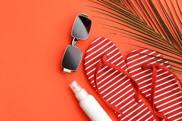 Flip-flops, sunglasses, bottle of sunscreen and palm leaf on red background