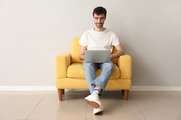 Poster - Young man working with laptop in armchair near light wall