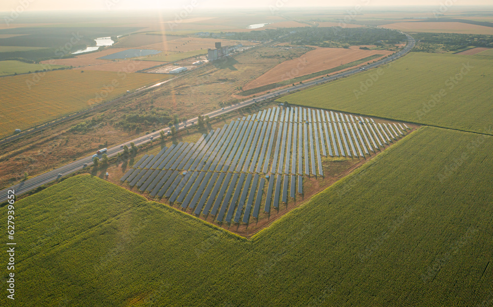 Solar panel park. Aerial photo with a big solar photovoltaic energy farm in the middle of an agriculture field during a summer sunrise. Green electricity industry concept image.