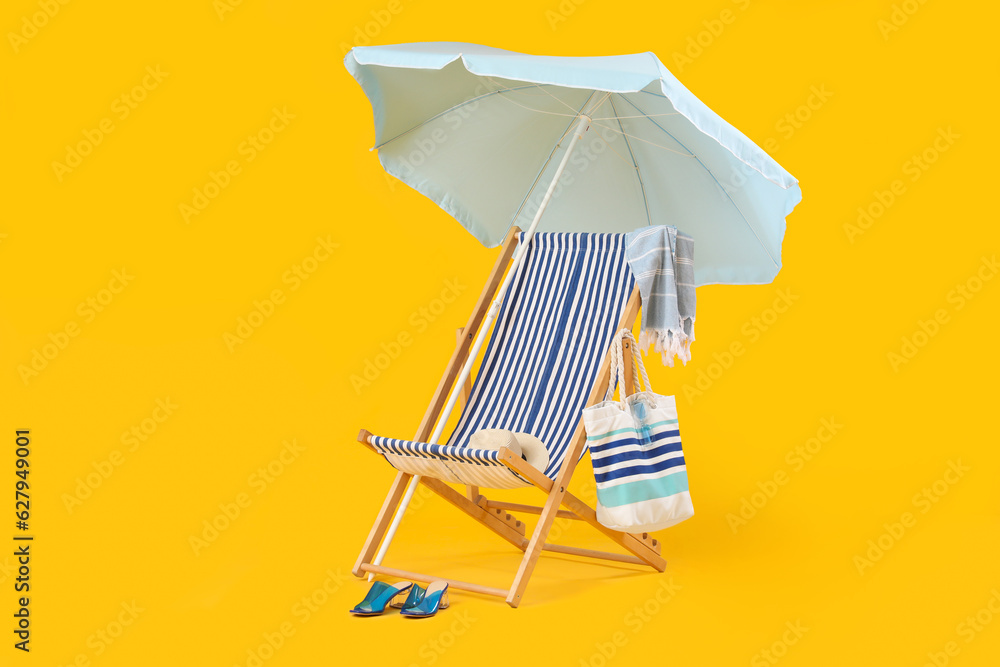 Deckchair with beach accessories and umbrella on color background