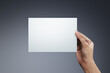 Woman hand holding a blank paper on gray background.