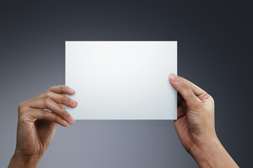 Wall Mural - Woman two hands holding a blank paper on gray background.