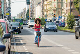 Fototapeta Miasto - Positive black woman riding electric bicycle on city street