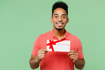 Wall Mural - Young fun man of African American ethnicity he wear pink t-shirt hold gift certificate coupon voucher card for store isolated on plain pastel light green background studio portrait. Lifestyle concept.