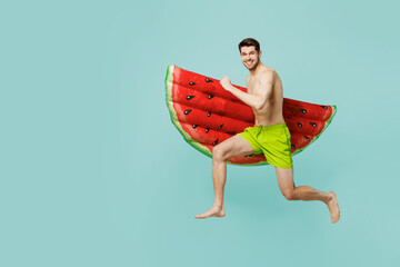 Full body side view young man wear green shorts swimsuit relax near hotel pool jump high with red inflatable rubber mattress isolated on plain blue background Summer vacation sea rest sun tan concept