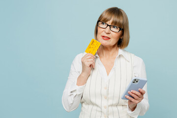 Wall Mural - Employee business woman 50s wears white classic suit glasses formal clothes use mobile cell phone hold credit bank card shopping online isolated on plain blue background. Achievement career concept.