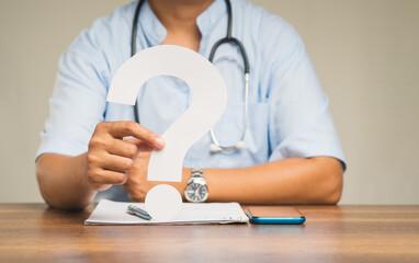 Physician holding a white question mark while sitting at the table in the hospital.