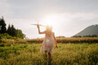 Little girl holding airplane toy during running in green field during warm summer day. Dream freedom concept. Playful cute little child pilot on background mountain and sky at amazing sunset