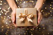 Close up of a woman holding a luxury gift box present wrapped with gold ribbon and golden glitter