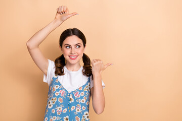 Wall Mural - Photo of cute dreamy girl dressed flower print overall looking pointing two thumbs empty space isolated beige color background