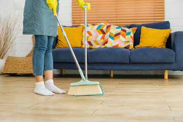 Crop image of a young professional cleaning service women worker working in the house. Girls housekeeper sweeps broomsticks on the wooden floor and cleaning under the sofa. Cleaner and chore concept