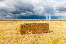 Wind Turbines Landscape Scenery And Grain Fields With Dramatic Sky. Hay Bales In Field. Storm Over The Field. Dark Clouds Are Gathering, Farmland With Wind Turbine. Storm Clouds Gather