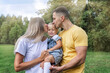 © Анна Демидова - Happy parents with their little daughter in the park on a sunny summer day. Laughing young woman with a man and a child in jeans and t-shirts hug and kiss. Love and tenderness.