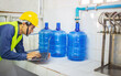 © NARONG - man worker and quality inspector using computer tablets check blue water gallons before shipment to contain drinking water.