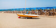 Small boat - sailboat , light brown
Dark orange color. He stands on a sandy beach, with blue umbrellas in the background. Format: panorama