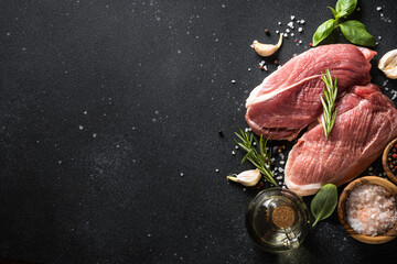 Wall Mural - Raw meat steaks with spices, herbs and oil at dark background. Top view with space for text.