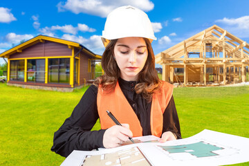 Wall Mural - Woman architect. Girl draws construction drawings. Architect near one-story buildings. Girl engineer corrects architectural plan. Woman in builder's uniform. Architect controls construction process