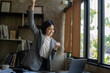 © Wasana - Happy asian bussiness woman celebrating victory while receiving good news on her labtop, excited about successful project.