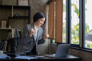 Happy asian bussiness woman celebrating victory while receiving good news on her labtop, excited about successful project.