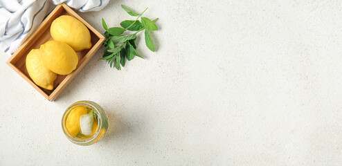 Wall Mural - Glass of ice tea, mint and wooden box with lemons on light background with space for text, top view