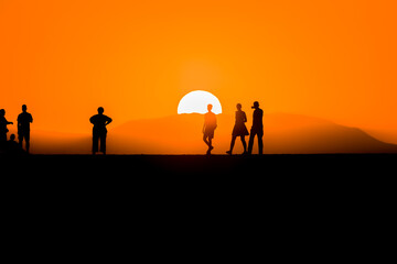 Wall Mural - Silhouette of tourists watching the sun set behind a distant mountain in summer