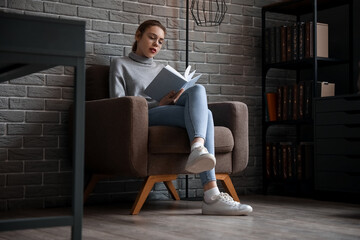 Poster - Young woman reading book in armchair at home