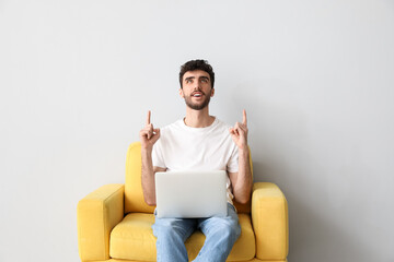 Sticker - Young man with laptop pointing at something in armchair on light background