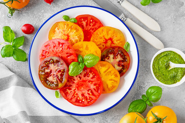 Wall Mural - Salad of colorful juicy tomatoes cut into slices with pesto sauce on a gray concrete background. Summer healthy salad.