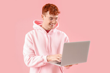 Young redhead man using laptop on pink background