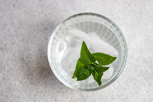 Glass Of Mineral Water With Ice Cubes And Fresh Mint Leaves Against Gray Background