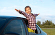 Happy little girl with her arms outstretched at open car window, her hair fluttering in wind. Travel concepts