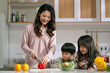 young asian mother making salad watched by her two children